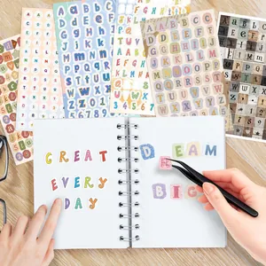 Detalle de pegatinas de letras de colores aplicadas a un cuaderno usando unas pinzas
