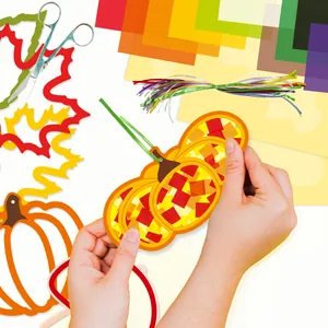 Mains tenant un attrape-soleil citrouille fini d'un kit de bricolage en papier enfant.