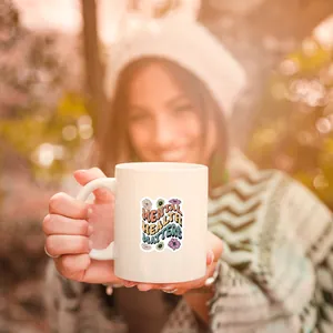 White ceramic mug featuring a Mental Health Matters sticker held in a sunny garden