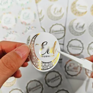 Detailed close-up of a decorative gold foil Eid moon sticker held with tweezers for gifting