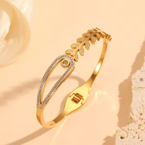 Detailed macro view of a gold stainless steel bangle featuring leaf motifs and crystal inlay