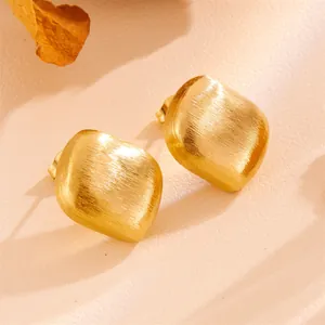 Detail of vintage geometric earrings with brushed gold finish on leather texture.
