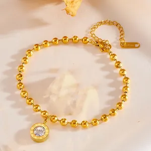 Detailed view of a golden stainless steel bead bracelet with Roman numeral crystal pendant