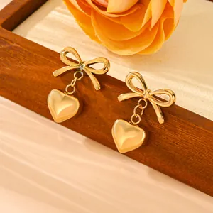 Detailed macro view of gold-plated stainless steel bow and heart dangle earrings