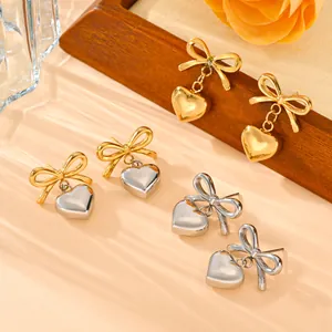 Close-up detail of stainless steel bowknot earrings with polished heart-shaped pendants