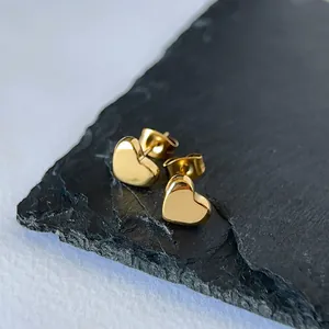 Close-up of minimalist gold heart stud earrings made of stainless steel on dark stone.