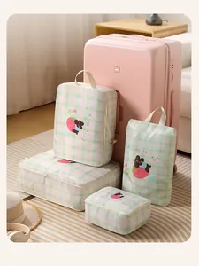 Detail shot of four green plaid travel packing cubes arranged around a pink suitcase