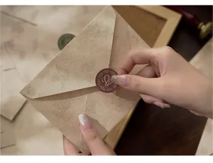 Close-up of a hand applying a vintage 'Love' sticker to a patterned kraft envelope