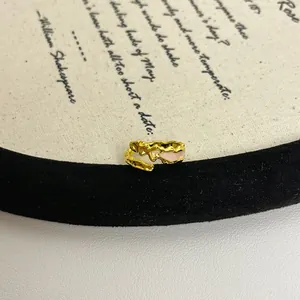 Nahaufnahme eines unregelmäßig strukturierten Goldrings mit zartrosa Emaillierung.