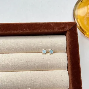 Close-up detail of light blue enamel star stud earrings displayed in a brown jewelry tray