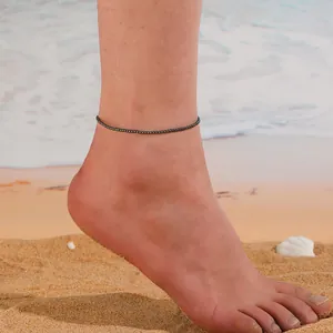 Détail d'une chevillère en perles sombres sur le pied d'un mannequin à la plage.