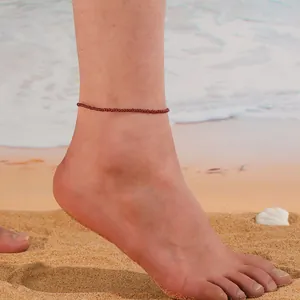 Gros plan d'une chevillère minimaliste en perles de cristal rouge sur la plage