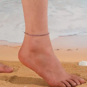 Gros plan d'une chevillère en perles de cristal naturel violet sur une cheville à la plage.