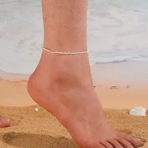 Gros plan d'un bracelet de cheville minimaliste à perles blanches sur une plage d'été.