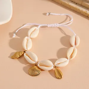 Close-up of handmade natural cowrie shell bracelet with gold-tone ocean charms on beige background