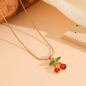 Detailed view of red cherry pendant with green leaf crystals on a gold snake chain necklace