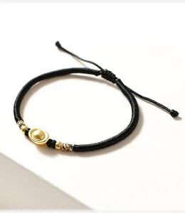 Dettaglio di un bracciale in corda nera intrecciata con una perla a forma di lingotto d'oro