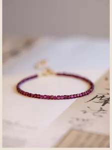 Dettaglio ravvicinato di perline di granato viola da 2mm su un bracciale sottile
