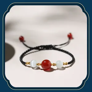 Detailed macro shot of red agate and cat's eye stone beads on a black braided bracelet.