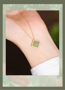 Macro shot of a square green Hetian nephrite jade pendant necklace worn on a woman's wrist.