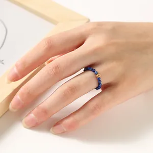 Detailed view of 2mm blue faceted beaded ring with small golden luck coin charm on hand