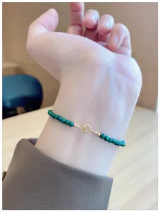 Close-up of thin natural green malachite beaded bracelet with gold clasp on wrist