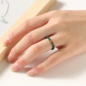 Macro detail of minimalist 2mm green beaded ring with S925 silver gold bead on finger.