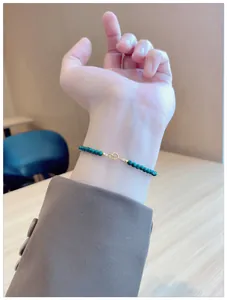 Delicate natural malachite beaded bracelet on a wrist with a grey suit sleeve.