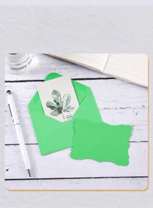 Detail view of a green wavy edge greeting card and matching envelope on wooden surface.