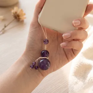 Close-up of a hand holding a natural purple amethyst crystal gourd phone charm