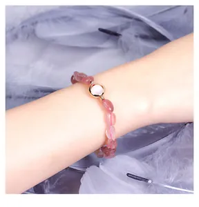 Detail shot of a pink strawberry crystal bead bracelet on a wrist with feathers background.