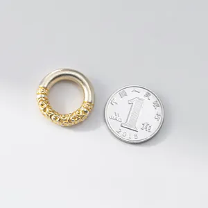 Primer plano de accesorio de anillo de plata 3D y chapado en oro junto a moneda.