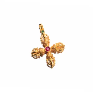 Close-up of intricate gold-plated silver cross vajra pendant with a red gemstone