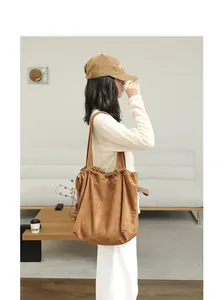 Side view of model carrying a large brown suede-look drawstring tote shoulder bag.