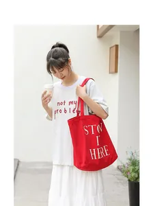 Borsa tote in tela rossa con stampa di lettere bianche indossata da una modella