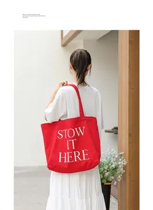 Dettaglio di una borsa tote in tela rossa con stampa di lettere portata da una modella.