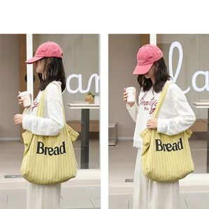 Detail view of yellow striped canvas tote bag with Bread letter print worn by model.