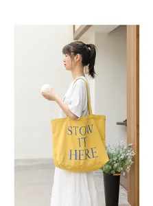 Foto lifestyle di una borsa tote in tela gialla con stampa a lettere blu STOW IT HERE