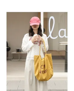 Sac cabas élégant en lin jaune avec imprimé lettré porté par un mannequin chic.