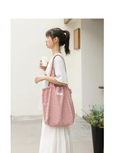 Bolso tote de lona rosa con lunares y cierre de cordón, llevado por una modelo al aire libre.