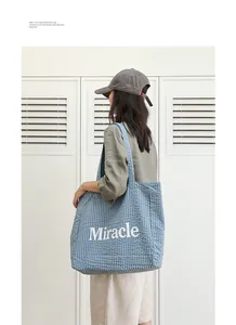 Detalle de un bolso tote de cuadros azules con el estampado Miracle blanco en nailon
