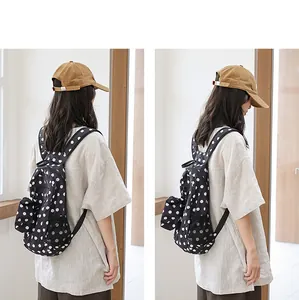 Vista trasera de una modelo con una mochila de nailon negro con lunares blancos.