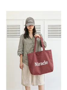 Primer plano de un bolso tote de cuadros granate con estampado Miracle llevado por modelo