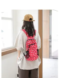 Detalle de una mochila de nailon roja con lunares blancos llevada por una modelo afuera