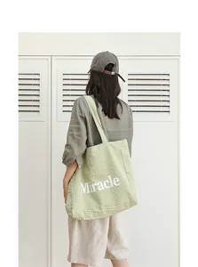 Vista trasera de una modelo con un bolso tote de lona verde claro con el estampado Miracle.