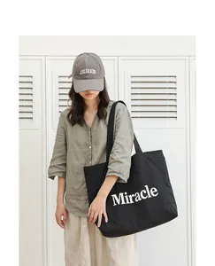 Primer plano de bolso tote de nailon negro con letras Miracle blancas en modelo