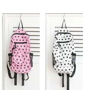 Vista detallada de mochilas de nailon con lunares rosas y blancos colgadas de ganchos de pared