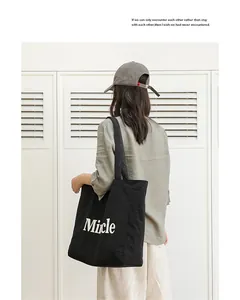 Vista trasera de un bolso tote de nailon negro con letras blancas llevado por modelo