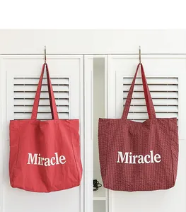 Vista detallada de bolsos tote de nylon rojo liso y a cuadros con el estampado Miracle