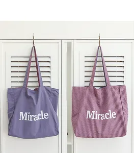 Comparación de un bolso tote de nailon morado liso y de cuadros con texto Miracle.